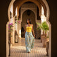 Female model wearing a Zendri yellow ruched top and blue floral maxi skirt, walking through an ornate sunlit archway.