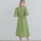 Back view of a flowing midi A-line wrap dress in sage green cotton gauze with voluminous short puff sleeves. The dress features an elasticated waistband and is paired with white sneakers.