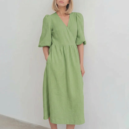 Zenia sage green crinkled cotton gauze midi wrap dress featuring voluminous puff sleeves and a tie waist, modeled against a neutral studio backdrop. This elegant dress offers a romantic, bohemian aesthetic.