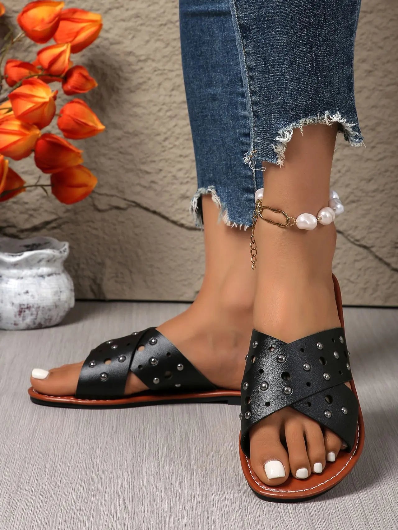 Zenoria black studded criss-cross strap slide sandals shown on feet with distressed denim jeans and a pearl anklet. Flat bohemian chic footwear for summer.
