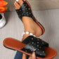 Black Zenoria studded slide sandals with criss-cross perforated straps and a tan faux leather footbed, shown worn on a model with a pearl ankle bracelet.