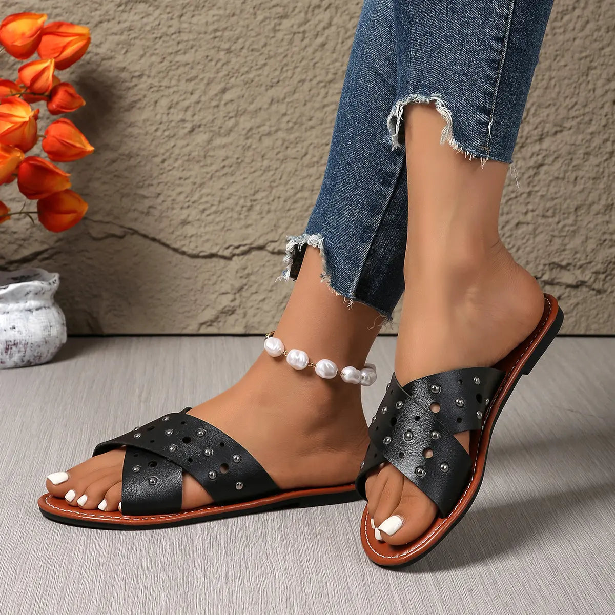 Black Zenoria studded criss-cross strap slide sandals worn by a model with distressed jeans and a pearl anklet, showcasing bohemian chic style.