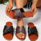 Zenoria studded slide sandals in black and brown with tan footbeds, featuring criss-cross perforated straps and silver-tone studs, displayed on a speckled studio floor with hands holding one pair.