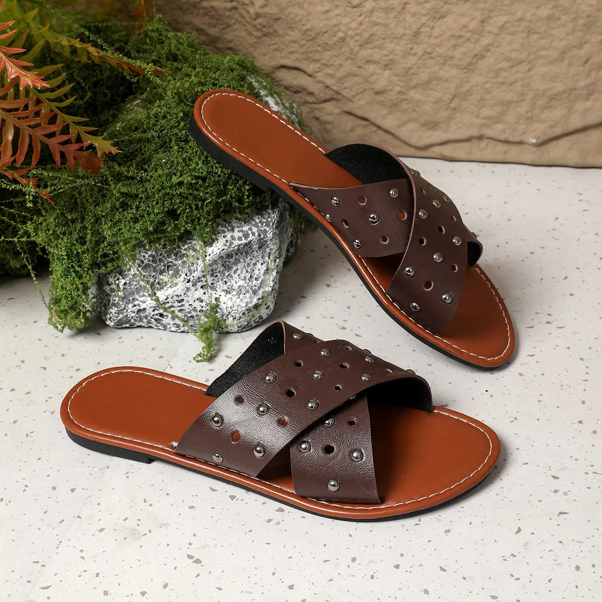 Brown Zenoria studded slide sandals with criss-cross perforated straps and tan faux leather footbeds, displayed as a pair on a studio background.