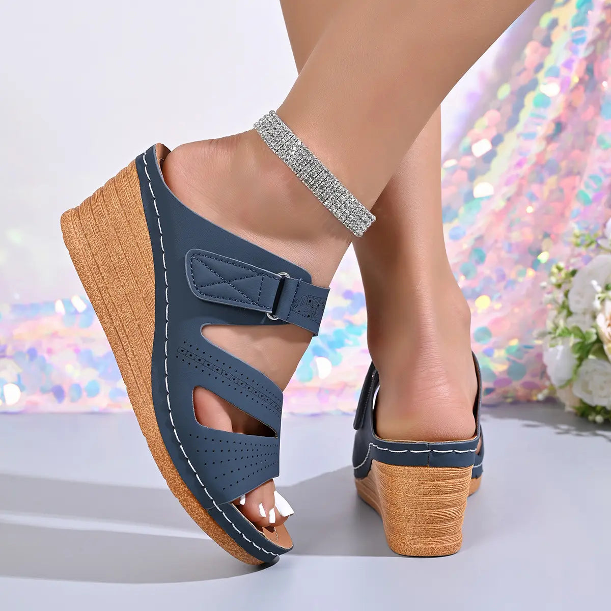 Dark blue perforated Zephira women's wedge sandals with peep-toe fish mouth, adjustable hook-and-loop strap, white contrast stitching, and wood-effect wedge heel, styled on a model with a sparkling anklet.