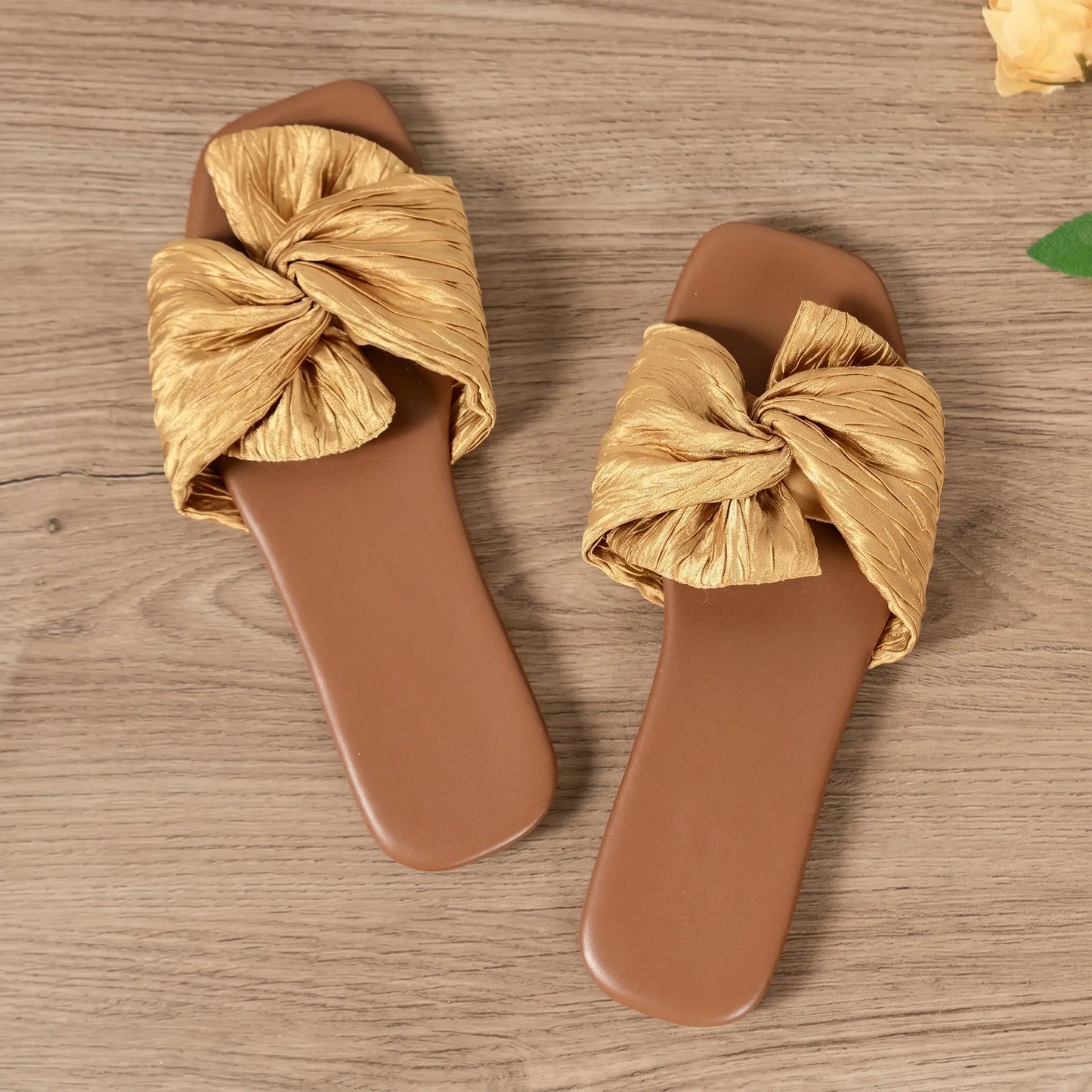 Champagne gold Zephyra women's flat slide sandals featuring a crushed satin bow and square toe, laid flat on a wooden surface.