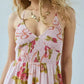 Bohemian floral print maxi dress on a model, featuring a smocked pink gingham bodice with a deep V-neck halter and a tiered skirt. Elegant summer fashion.