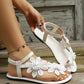 A woman's feet wearing white Zephyra floral lace flat sandals with delicate appliques and an adjustable ankle strap, styled on weathered wooden planks.