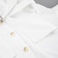 Close-up of an optic white Zephyra playsuit showing pearlescent buttons, chest flap pocket, and matte fabric texture.