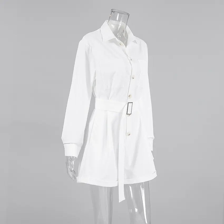 Zephyra elegant white playsuit with shirt collar, long cuffed sleeves, button-down front, chest pockets, and a gold-buckled belt cinching the waist. Tailored shorts shown on a mannequin from a three-quarter angle.