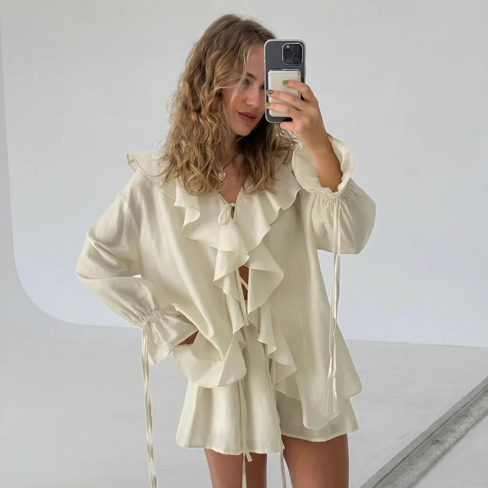 Model wearing an ivory cream boho ruffle summer set featuring a voluminous tiered ruffle blouse with a tie V-neck and balloon sleeves, paired with high-waisted drawstring shorts. Photographed from the front in a studio.
