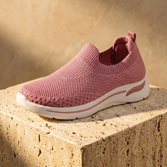 Zhivra women's dusty rose knit slip-on sneaker, shown in a three-quarter view, featuring a breathable perforated upper, ribbed collar, and thick white wedge sole with a pink side accent, resting on a textured light brown block.