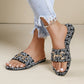 Black Zirali logo slide sandals with ornate gold-tone buckle, worn by a model with distressed denim jeans in a lifestyle setting.