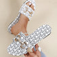 Zirali women's white slide sandals featuring an all-over black logo print and ornate gold-tone buckle hardware, shown on a foot with rings and held by a hand.