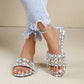 White Zirali logo slide sandals with black monogram print and ornate gold-tone buckles, worn on feet with distressed jeans.