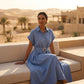 Woman in Zivro chambray blue belted linen midi dress with gold buckle, sitting in a desert resort setting.