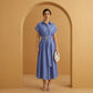 Model wearing a Zivro chambray blue linen-blend A-line midi dress, featuring a point collar, cuffed short sleeves, and a wide fabric belt with an organic gold-tone buckle, presented against a warm studio archway.