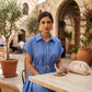 Model wearing a Zivro chambray blue belted linen-blend A-line midi dress with gold-tone buckle, enjoying coffee at an outdoor cafe.