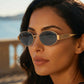 A woman wears Zokari classic gold and smoke grey oval metal frame sunglasses outdoors with a blurred scenic background, showcasing the vintage bohemian style and UV400 protection.