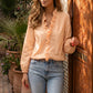 Elegant model in a Warm Apricot ruffled V-neck blouse with long blouson sleeves, paired with light jeans, leaning on a carved wooden door.