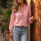 Model wearing a Zokiru romantic blush pink ruffled V-neck long sleeve blouse, styled casually with jeans, in an elegant outdoor setting with a carved wooden door.