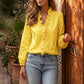 Model wears a Zokiru sunshine yellow ruffled V-neck blouse with long voluminous sleeves and light wash jeans, posing next to an ornate wooden door in an outdoor setting.