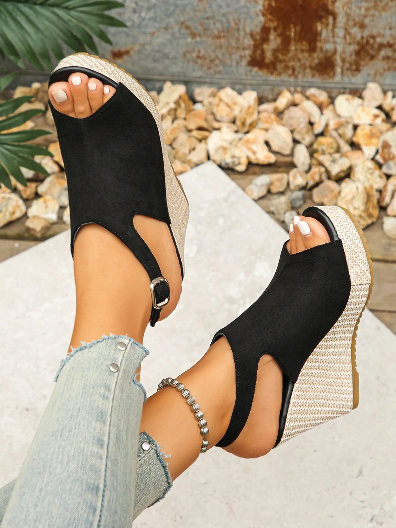 Black peep-toe espadrille wedge sandals worn by a woman, showcasing the jute-wrapped extra-high wedge heel, adjustable ankle strap, and matte suede-like upper material.