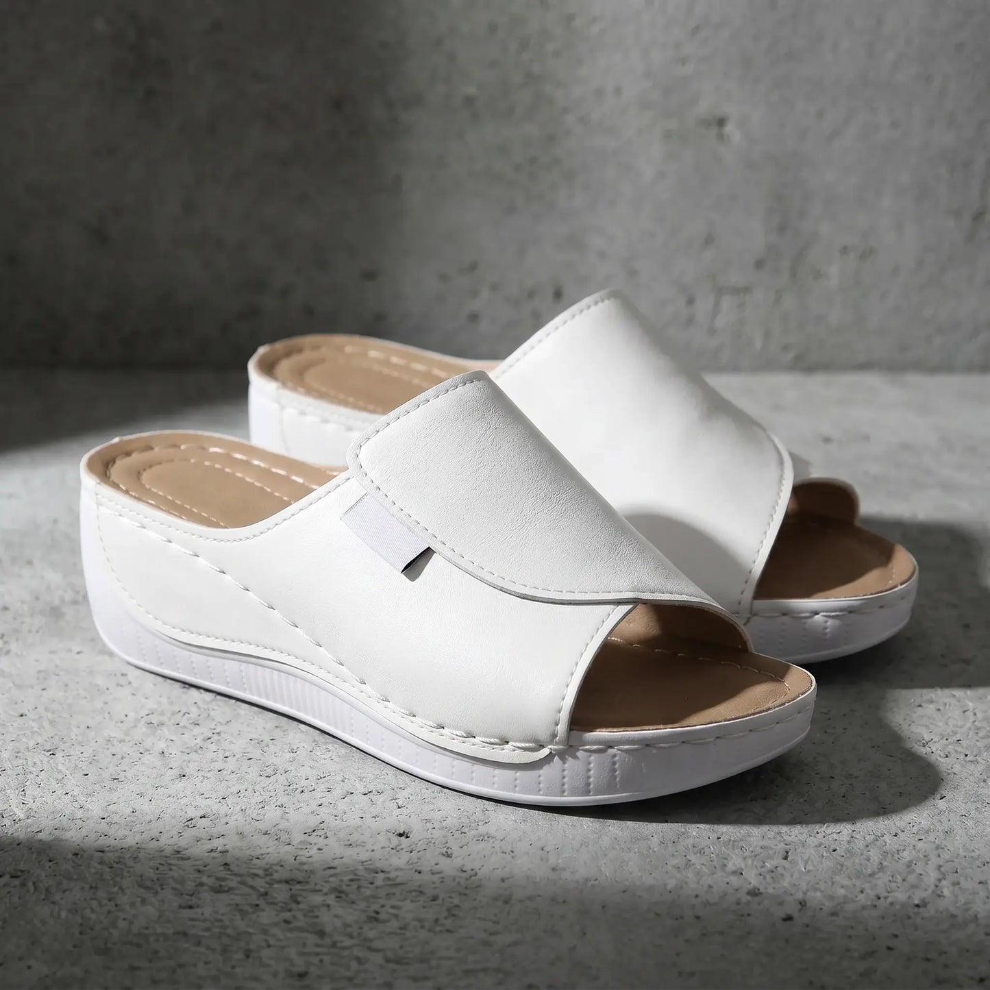 White Zoltar women's slide sandals featuring an open toe, single wide strap, and a layered wedge sole with subtle contrast stitching, shown at a three-quarter angle.
