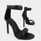 Black Zoltra strappy stiletto sandals with puffy toe and ankle straps, pointed toe, and back zipper detail, shown in a three-quarter view.
