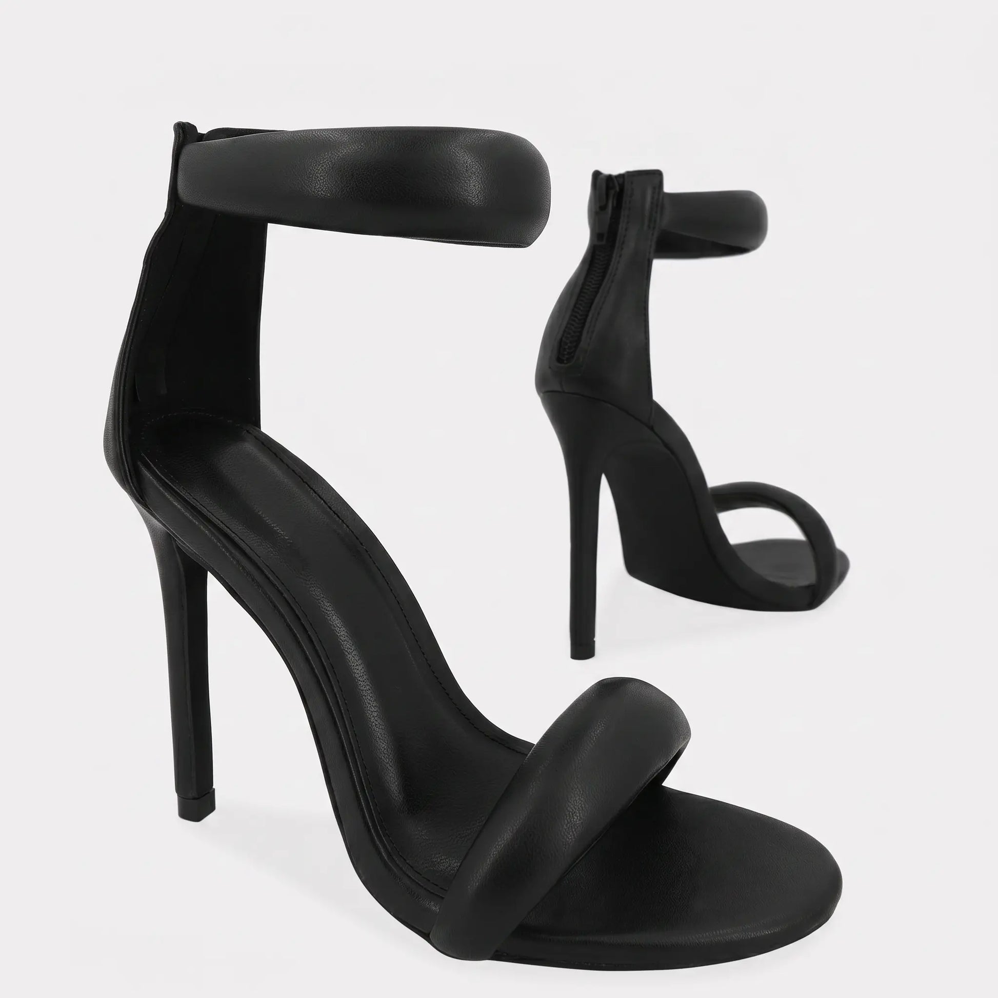 Black Zoltra strappy stiletto sandals with puffy toe and ankle straps, pointed toe, and back zipper detail, shown in a three-quarter view.
