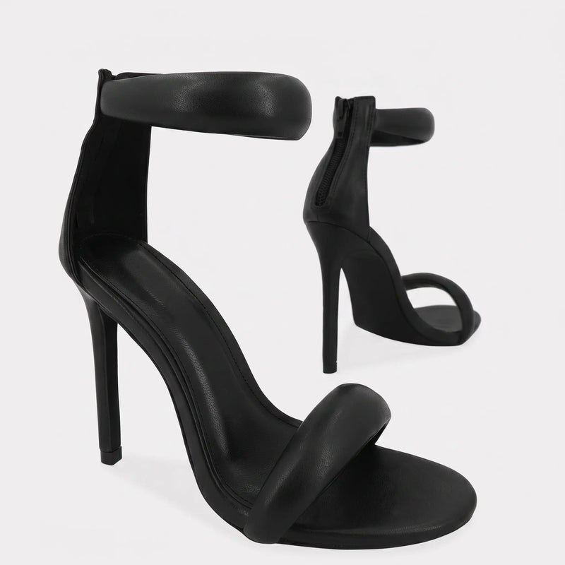 Black Zoltra strappy stiletto sandals with puffy toe and ankle straps, pointed toe, and back zipper detail, shown in a three-quarter view.