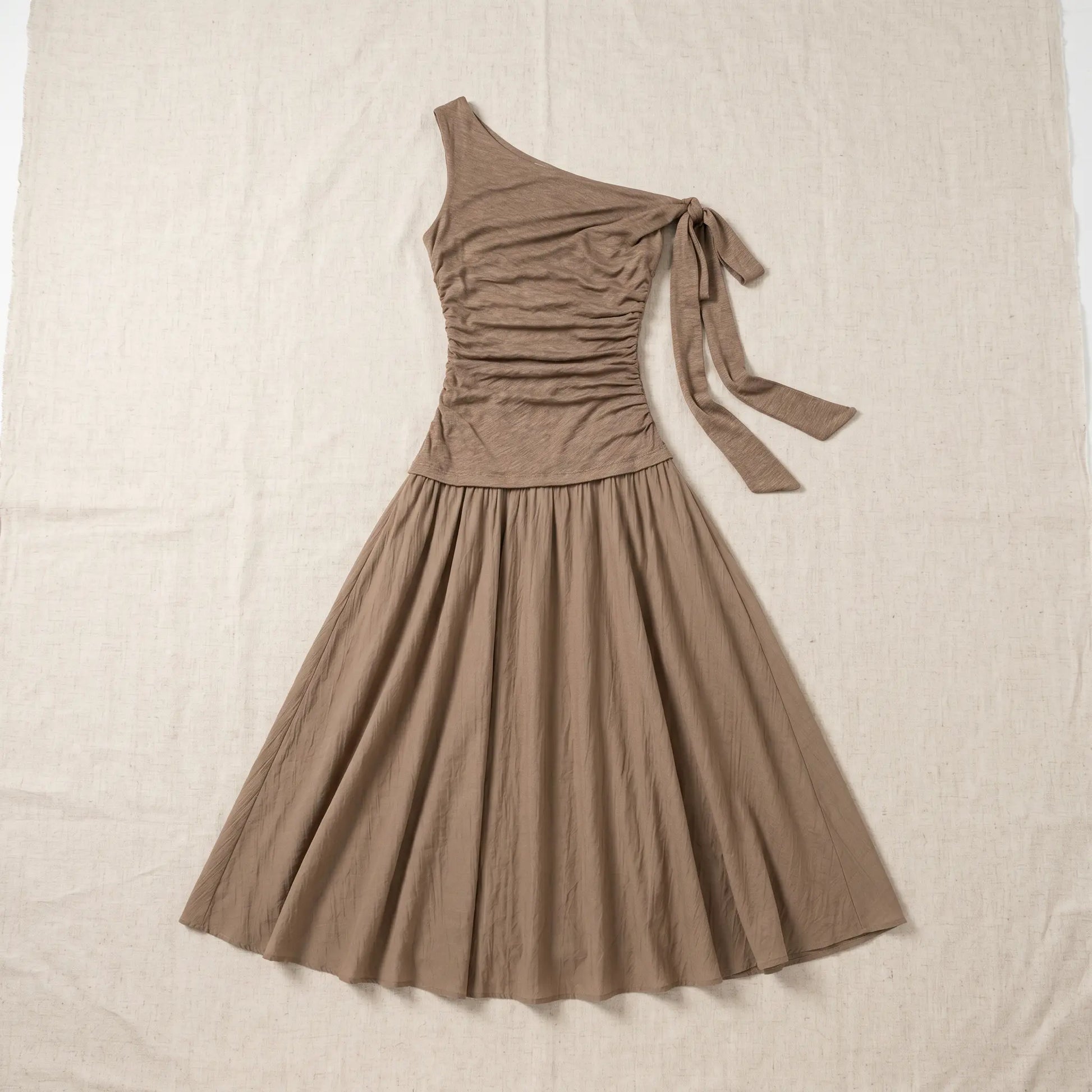 Zolwen coffee taupe asymmetric ruched drop-waist maxi dress, featuring a one-shoulder tie and flowing crinkled A-line skirt, presented in a flat-lay view.