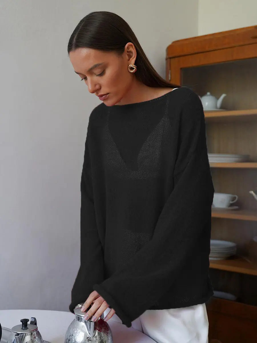 Female model wearing a Zomari black semi-sheer knit sweater with long bell sleeves and a wide boat neck in a relaxed indoor setting.