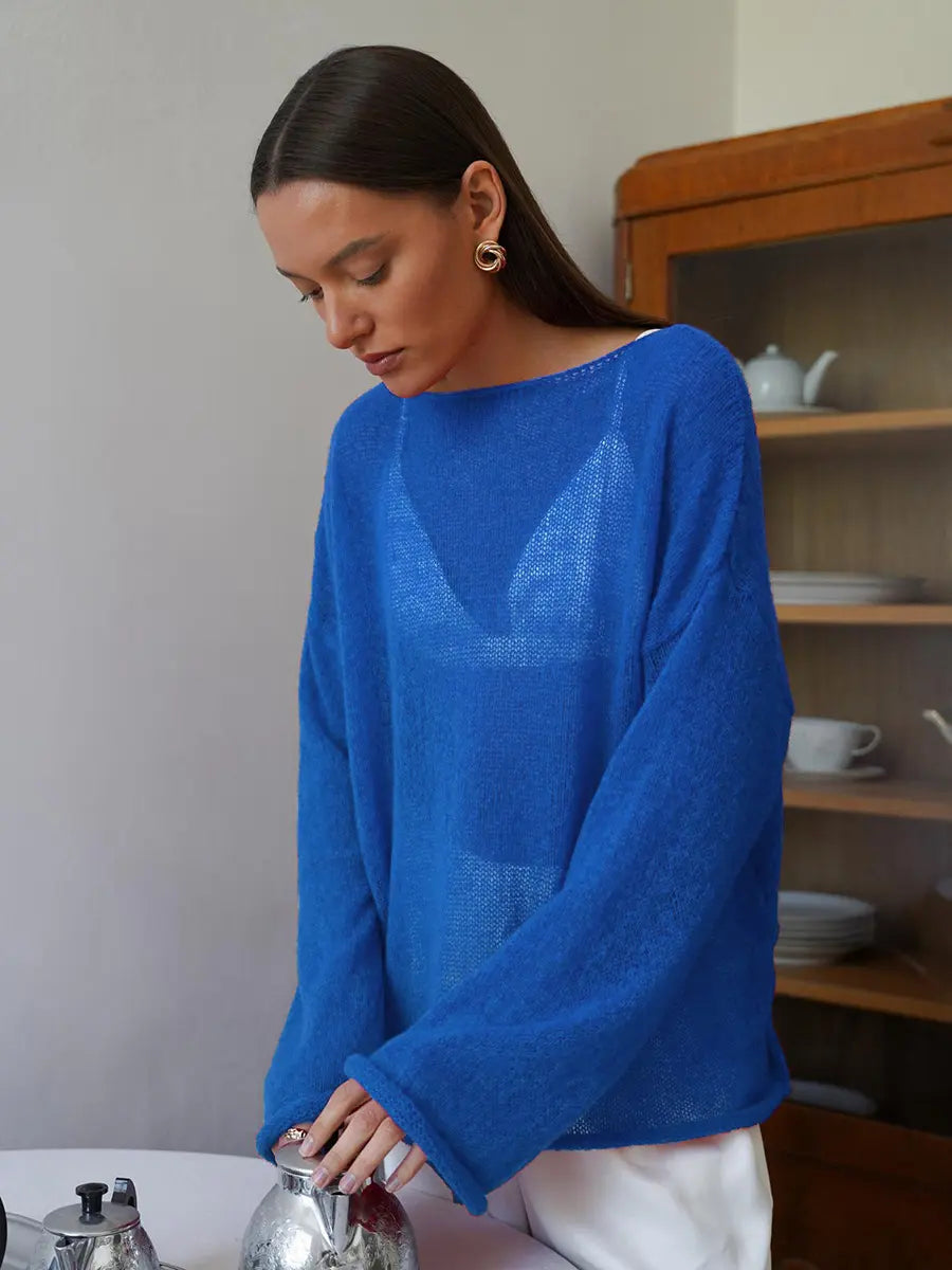 Model wearing a vibrant blue Zomari sheer bell sleeve knit sweater with an open-knit texture and boat neck, styled in a relaxed indoor setting.