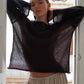 Female model wearing Zomari charcoal grey semi-sheer knit sweater with bell sleeves and dropped shoulders, styled in an elegant indoor setting.