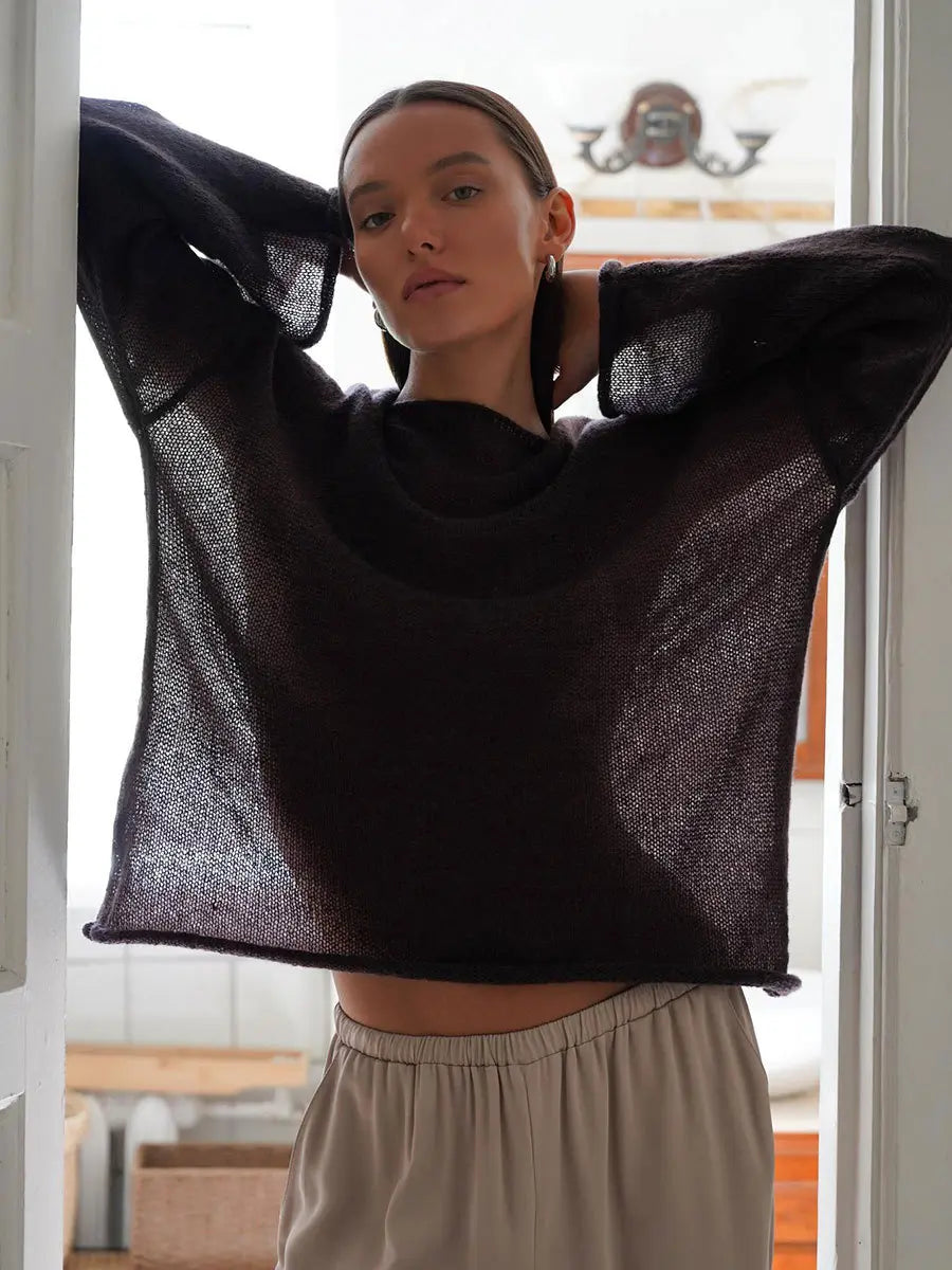 Female model wearing Zomari charcoal grey semi-sheer knit sweater with bell sleeves and dropped shoulders, styled in an elegant indoor setting.