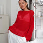Model wears a Zomari crimson red sheer bell sleeve knit sweater, showcasing its relaxed open-knit texture and wide boat neck in an elegant indoor setting.