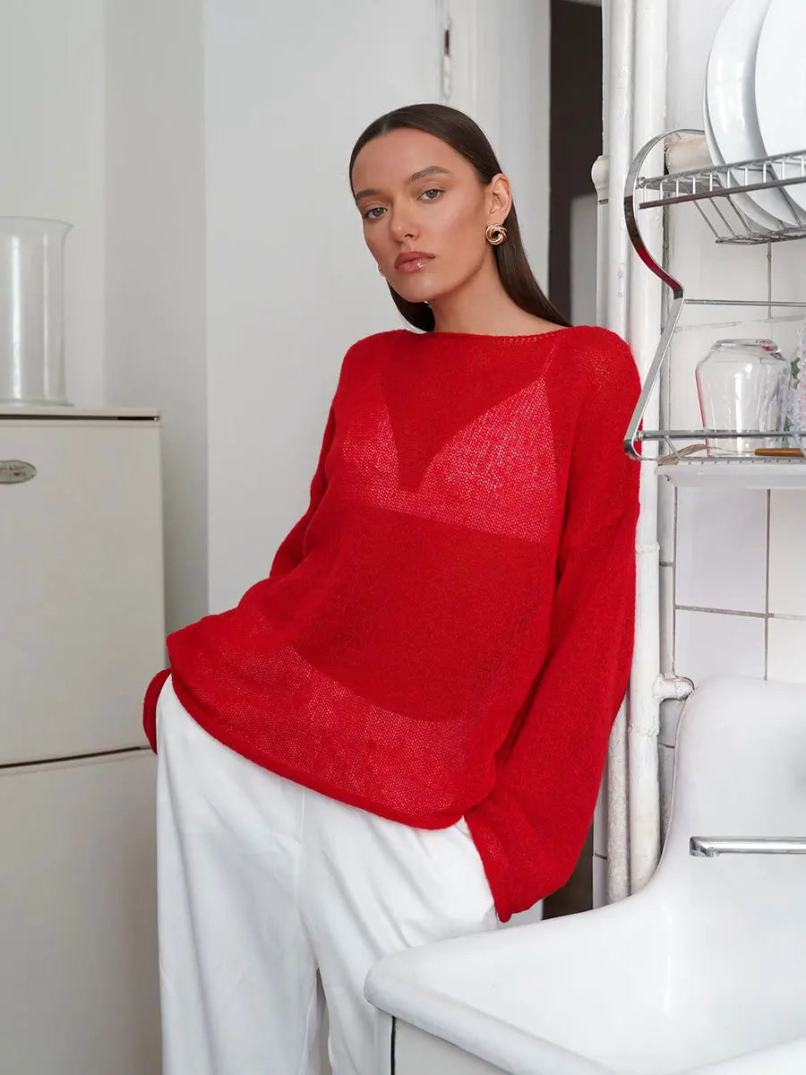 Model wears a Zomari crimson red sheer bell sleeve knit sweater, showcasing its relaxed open-knit texture and wide boat neck in an elegant indoor setting.
