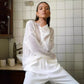 Female model poses wearing a Zomari Pristine White sheer knit sweater, showcasing its relaxed fit, wide boat neckline, and translucent open-knit texture. This lifestyle image highlights its effortless style.