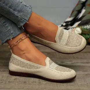 Women's warm beige Zoria knit loafers with crystal-embellished vamp and geometric pattern, shown on foot with denim jeans. Side view.