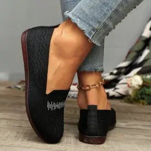 Zoria black knit loafers with subtle crystal embellishment on the vamp, worn on a person's foot with denim jeans against a lifestyle background.
