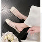 A pair of soft off-white mesh mules with a square toe, worn on a foot against a dark wood floor and styled with white fabric and flowers. Features airy diamond-patterned mesh and a subtle insole detail.
