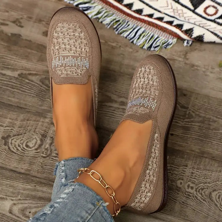 Lifestyle shot of women's beige breathable knit loafers with geometric pattern and crystal embellishments, worn with denim jeans and a gold anklet.
