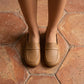Elegant Zoryn 'Soft Apricot' vegan leather slip-on loafers, featuring a classic transverse vamp strap and round toe, worn by a woman standing on textured terracotta tiles.