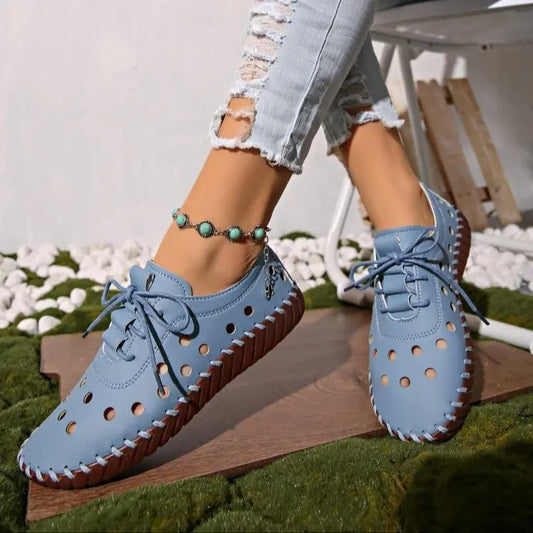 Close-up of a woman's foot wearing blue perforated Zoryn loafers with lace-up closure and contrasting stitching, styled with ripped jeans and a beaded anklet.