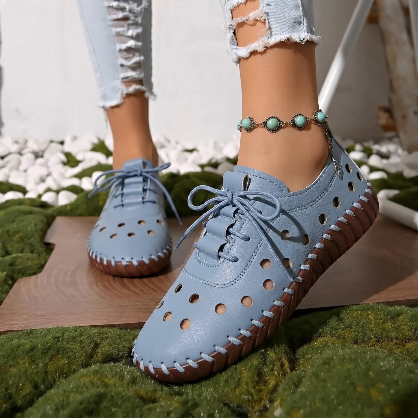 Dusty blue perforated lace-up flat loafers on a model's foot, styled with distressed jeans and a bohemian anklet, showcasing a casual, airy aesthetic.