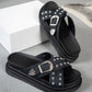 Black Zoryn platform slide sandals adorned with silver studs and ornate buckles, shown from a three-quarter angle on a grey studio floor.
