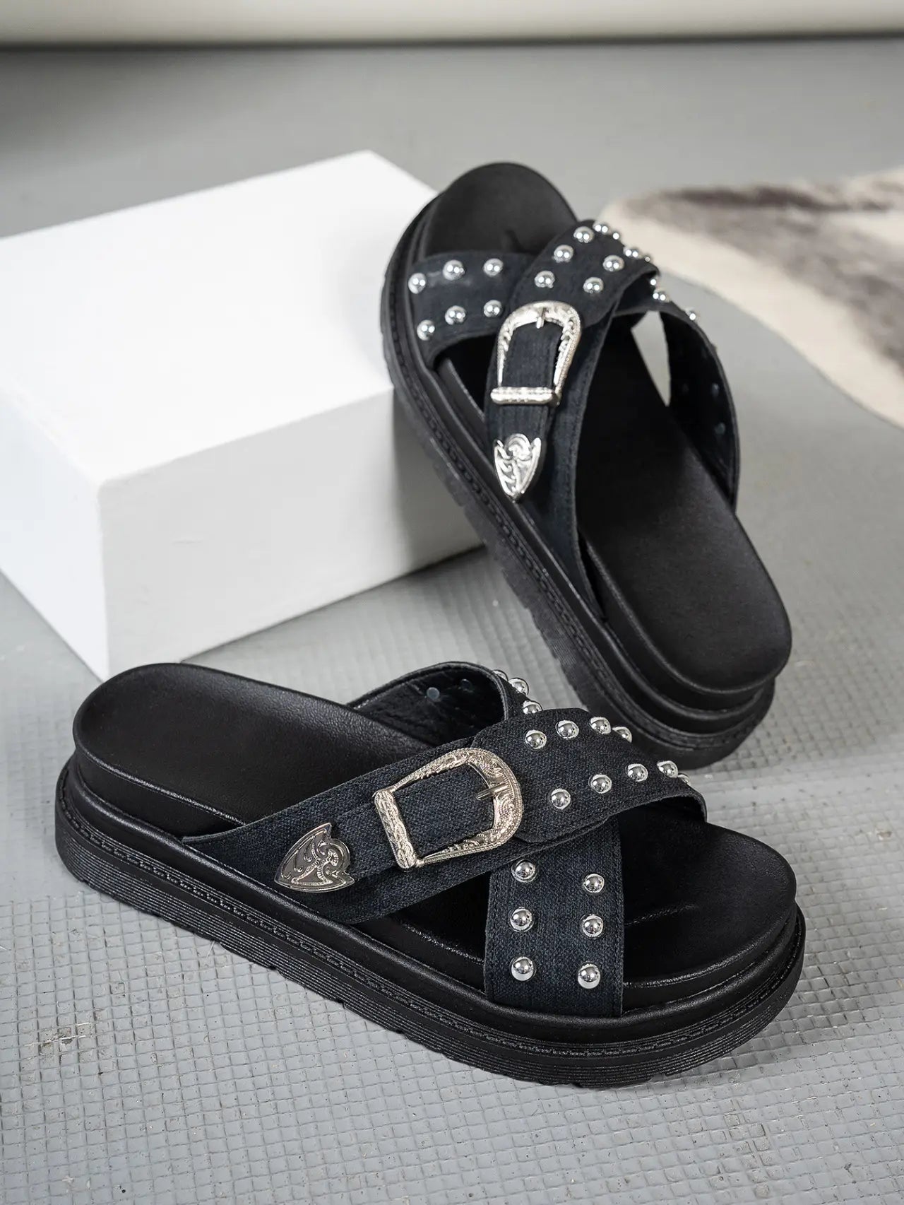 Black Zoryn platform slide sandals adorned with silver studs and ornate buckles, shown from a three-quarter angle on a grey studio floor.