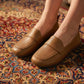 Classic Zoryn tan vegan leather slip-on loafers with a round toe and distinctive vamp strap, worn by a woman on a patterned rug.