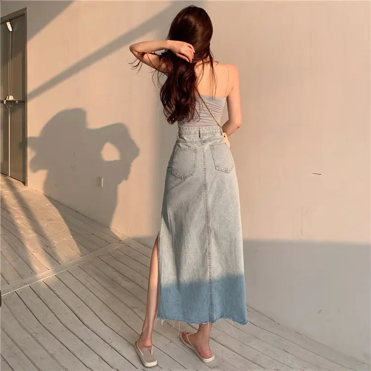 Woman from behind showcases a Zubari vintage light blue high-waisted A-line denim maxi skirt with a dramatic side slit, raw frayed hem, and classic rear patch pockets, exuding effortless bohemian elegance.